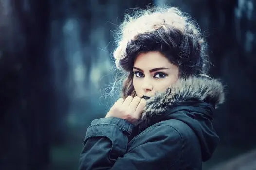 Frau mit dunklen Haaren und Augen in Winterjacke vor dunklem Hintergrund